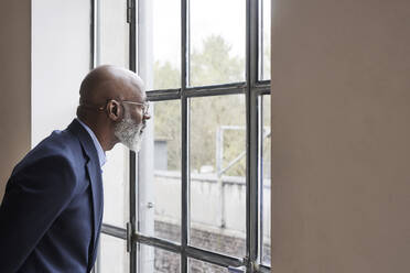 Businessman looking through window at home - FMKF07487