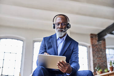 Geschäftsmann mit Headset, der zu Hause einen Tablet-PC mit digitalem Stift benutzt - FMKF07502