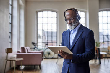 Businessman with headset working on tablet computer at home - FMKF07504