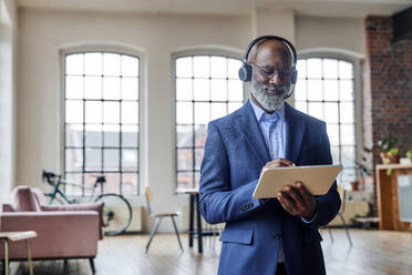 Smiling businessman with headset using tablet computer at home - FMKF07505