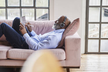 Geschäftsmann mit Headset, der einen digitalisierten Stift auf einem Tablet-PC im Wohnzimmer benutzt - FMKF07531