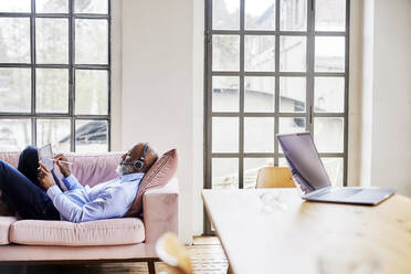 Businessman with headset working on tablet computer in living room - FMKF07532