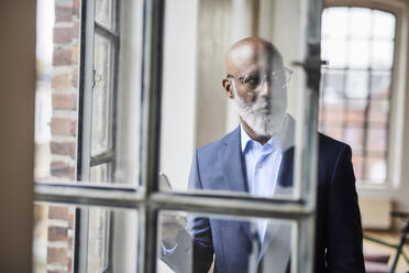 Thoughtful businessman seen through window at home - FMKF07547