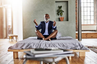 Mature businessman meditating on bed in bedroom at home - FMKF07561