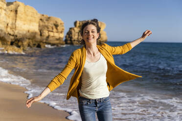 Glückliche Frau mit ausgestreckten Armen genießt vor dem Meer am Strand - DIGF17852