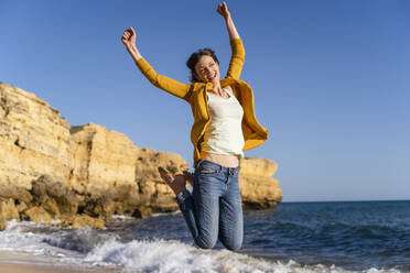 Excited woman jumping in front of sea at beach - DIGF17854