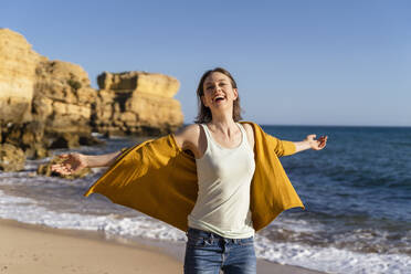 Glückliche Frau mit ausgestreckten Armen genießt am Strand an einem sonnigen Tag - DIGF17858