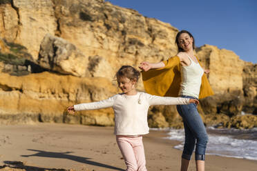 Happy woman with daughter enjoying at beach on sunny day - DIGF17859