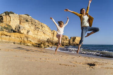 Glückliche Frau mit Tochter springt am Strand an einem sonnigen Tag - DIGF17861