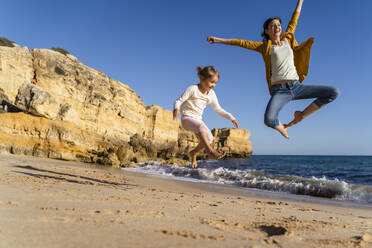 Glückliche Mutter mit Tochter springt am Strand an einem sonnigen Tag - DIGF17862