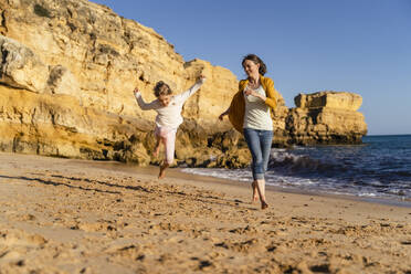 Glückliche Mutter mit Tochter läuft am Strand - DIGF17864