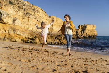 Happy mother with daughter running on shore at beach - DIGF17864