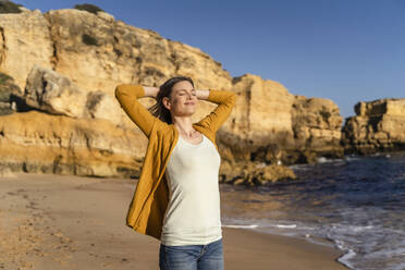 Smiling woman with eyes closed standing at beach - DIGF17865