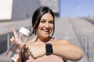 Glückliche Frau mit Wasserflasche und Smartwatch vor einer Treppe - EIF04050