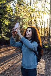 Woman using smart phone with augmented icons in forest - EGHF00386