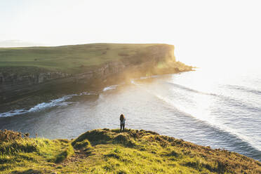 Young woman standing at coast looking at sea - EGHF00387