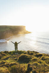 Young woman with arms outstretched standing at coast by the sea - EGHF00388