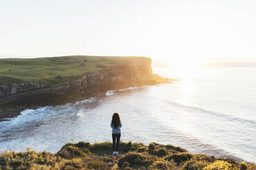 Woman standing at coast looking at sunset over sea - EGHF00389