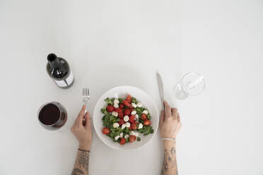 Hände einer Frau halten Besteck an einer Salatschüssel und Wein auf einem weißen Tisch - VPIF05983