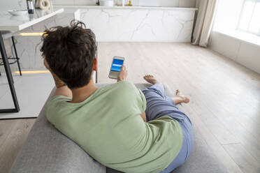 Woman using smart phone sitting on sofa at home - VPIF05996