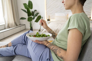 Frau isst Salat auf dem Sofa sitzend zu Hause - VPIF06003