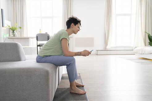 Frau, die ein Mobiltelefon benutzt, sitzt zu Hause auf dem Sofa - VPIF06013