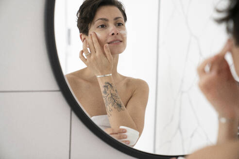 Frau trägt Feuchtigkeitscreme auf und betrachtet den Spiegel im Badezimmer - VPIF06024