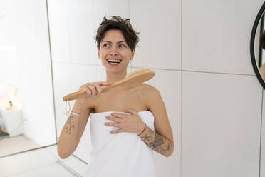 Happy woman wrapped in towel holding brush - VPIF06027