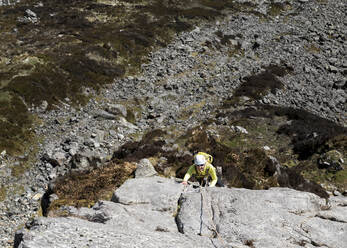 Ältere Frau mit Helm klettert an einem sonnigen Tag auf eine Felswand - ALRF01877