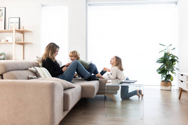 Seitenansicht von niedlichen barfuß Kinder versuchen, die Aufmerksamkeit der Mutter Surfen Tablet auf bequemen Sofa in hellen Wohnzimmer zu Hause zu bekommen - ADSF34570