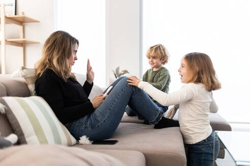 Seitenansicht von niedlichen barfuß Kinder versuchen, die Aufmerksamkeit der Mutter Surfen Tablet auf bequemen Sofa in hellen Wohnzimmer zu Hause zu bekommen - ADSF34571