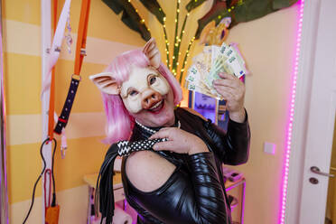 Happy transvestite man wearing pig mask holding whip and paper currency - JATF01335