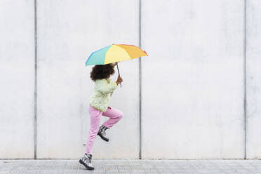 Mädchen genießt es, einen Regenschirm zu halten und läuft an einer weißen Wand vorbei - PNAF03790