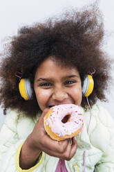 Afro girl with headphones eating doughnut - PNAF03816