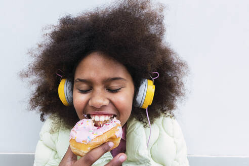 Girl with headphones eating doughnut - PNAF03817