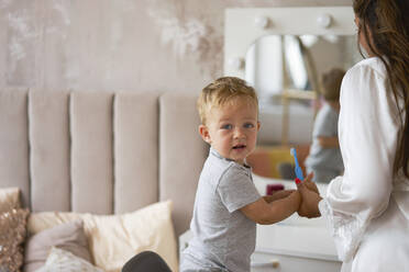 Junge schaut über die Schulter und hält die Zahnbürste seiner Mutter zu Hause - SSGF00843