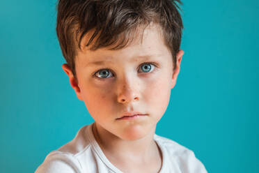 Headshot of upset boy with brown hair looking at camera with upset face expression while standing in light studio on green background - ADSF34626