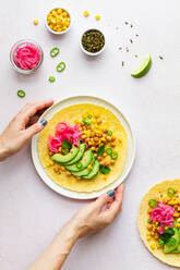 Hand of crop anonymous female touching tasty taco with ripe avocado slices and chickpea filling served on table - ADSF34673