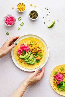 Die Hand einer anonymen Frau berührt einen leckeren Taco mit reifen Avocadoscheiben und Kichererbsenfüllung, der auf dem Tisch serviert wird - ADSF34673