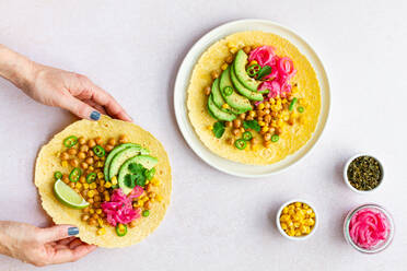 Die Hand einer anonymen Frau berührt einen leckeren Taco mit reifen Avocadoscheiben und Kichererbsenfüllung, der auf dem Tisch serviert wird - ADSF34675