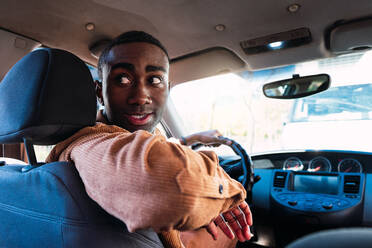 Emotionsloser afroamerikanischer männlicher Fahrer, der beim Rückwärtsfahren im Auto in der Stadt nach hinten schaut - ADSF34687