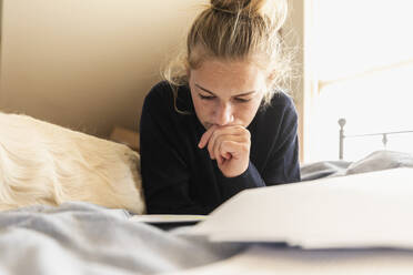 Teenage girl (16-17) lying on bed with dog and reading - TETF01632