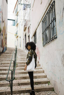 Glückliche junge Frau mit lockigem Haar auf einer Treppe stehend - DCRF01128