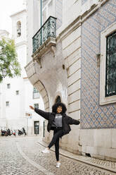 Playful woman standing with arms outstretched on footpath - DCRF01130