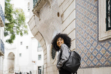 Lächelnde junge Frau mit Rucksack vor einem Gebäude stehend - DCRF01132