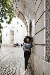 Happy young woman with hand in hair leaning on wall - DCRF01134