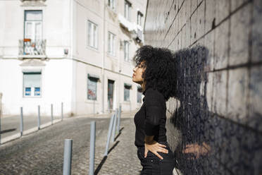 Frau mit Hand auf der Hüfte vor einer Mauer stehend an einem sonnigen Tag - DCRF01142