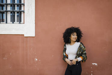 Smiling young woman with hand in pocket standing by wall - DCRF01148