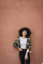 Smiling woman with hand in pocket leaning on wall - DCRF01149