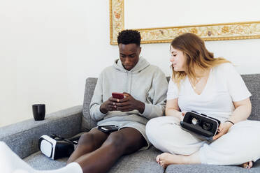 Young man using smart phone sitting by girlfriend on sofa at home - MEUF05326